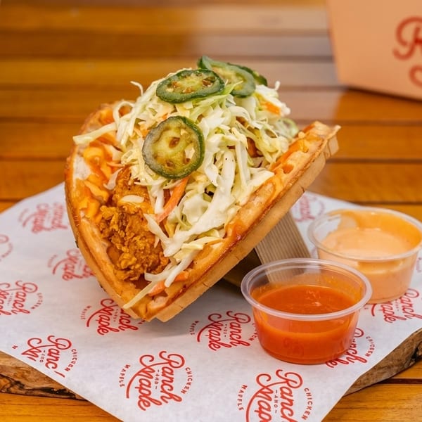 Ranch & Maple chicken and waffle sandwich with slaw, jalapeños, sauces, and a drink.