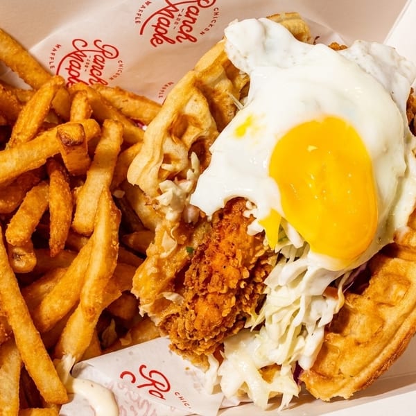 Chicken and waffle sandwich with a fried egg and coleslaw, served with a side of fries.