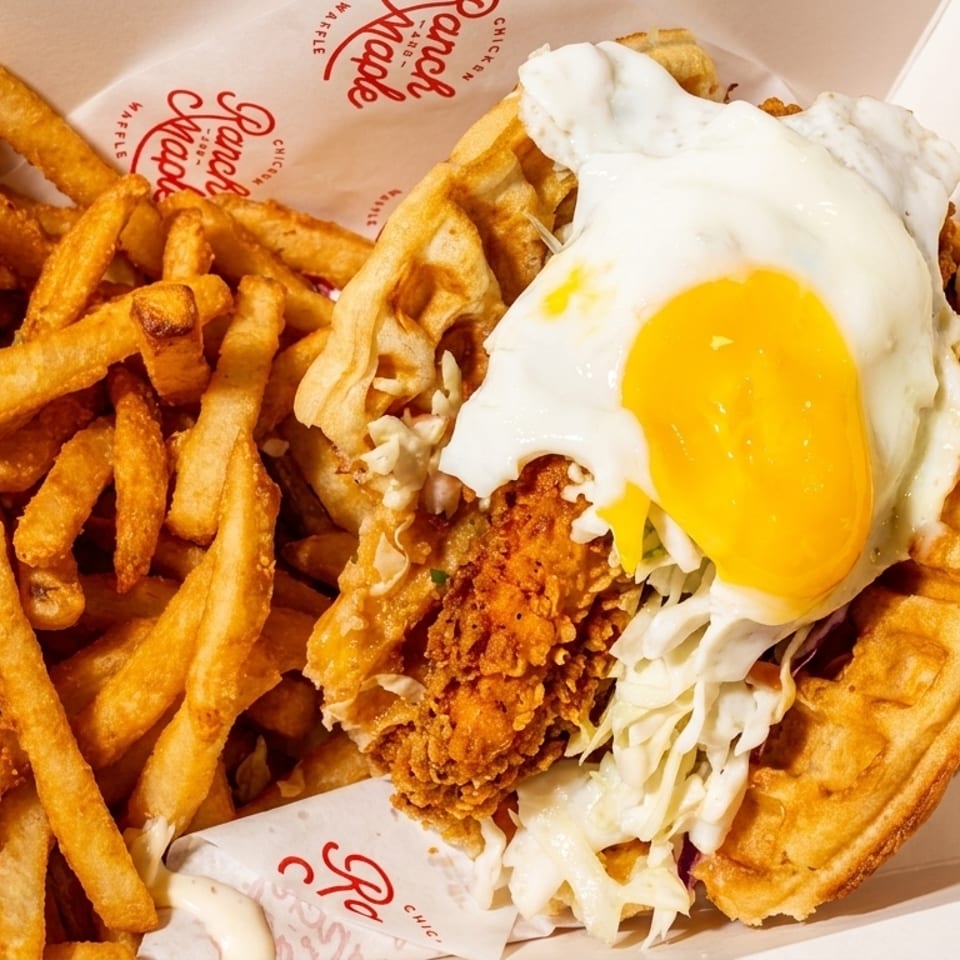 Chicken and waffle sandwich with a fried egg and coleslaw, served with a side of fries.