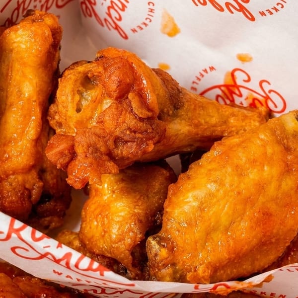 Close-up of several crispy, saucy chicken wings in a paper-lined box from "Brunch and Maple".